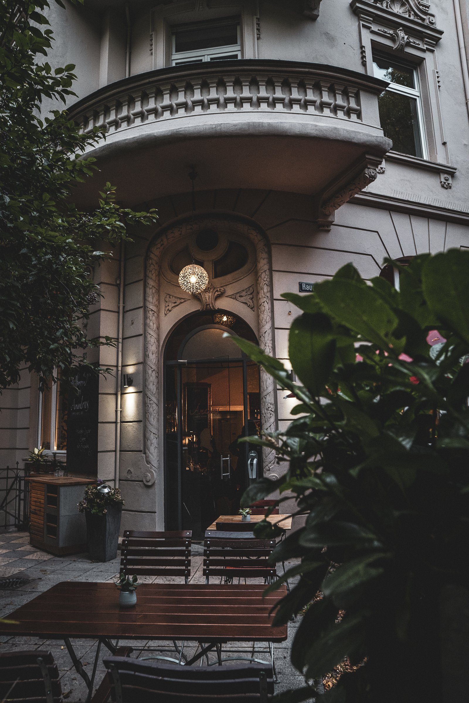 Der Eingang des Amadeus im Rheingauviertel — Altbaufassade mit Stuck, Laterne und Terrasse